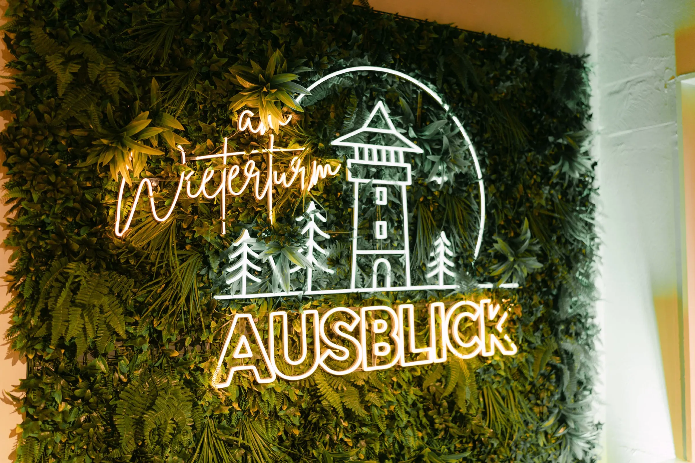 Goldene Neon-Schrift „Ausblick am Wieterturm“ auf einer üppigen Mooswand